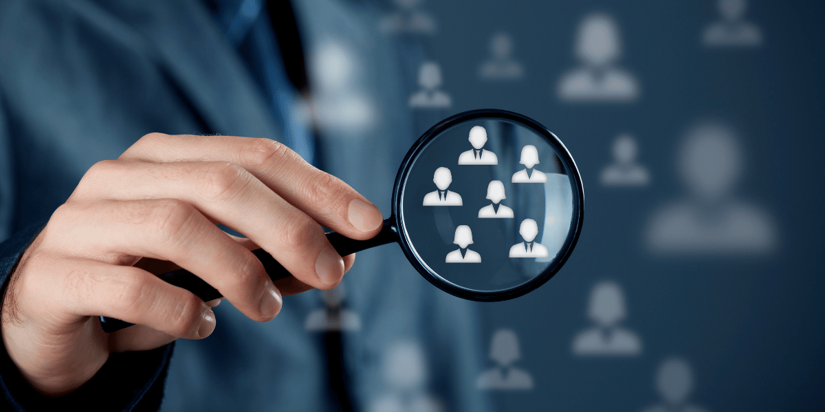 Hand using a magnifying glass to highlight customer profiles, representing multi-touch attribution.