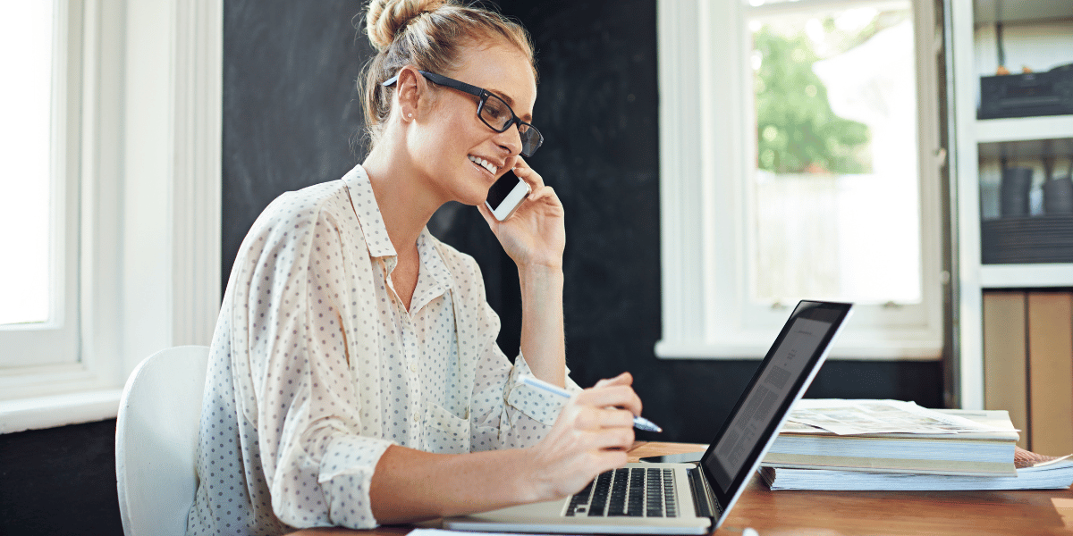 Business professional speaking on the phone while working at a laptop during a client call.